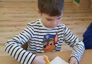 Chłopiec wycina koronę z papieru.